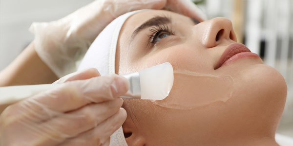 Beautician applying facial cream on young woman face skin in Sycamore, IL | Nuvo Aesthetics Clinic